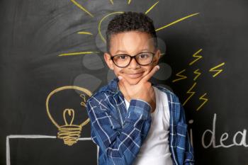 Thoughtful African-American boy near drawn light bulb on dark wall�