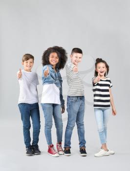 Stylish children in jeans showing thumb-up gesture on grey background�