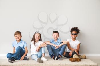 Stylish children in jeans sitting near light wall�