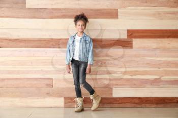 Stylish African-American girl in jeans clothes near wooden wall�
