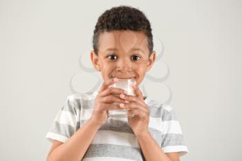 Cute African-American boy with glass of milk on white background�