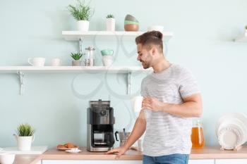 Handsome man using coffee machine in kitchen�