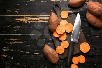 Cutting board and knife with raw sweet potato on wooden background�