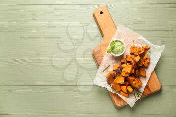 Board with tasty cooked sweet potato and sauce on wooden table�