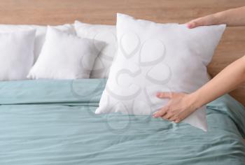 Woman fluffing soft pillows on bed�