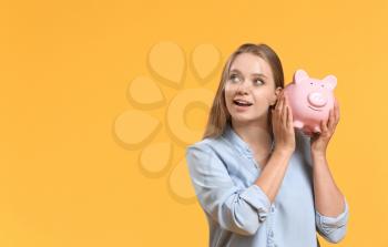 Young woman with piggy bank on color background�