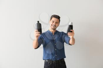 Handsome man with bottles of shampoo on light background�