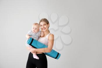 Sporty mother with cute little baby on light background�