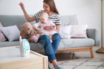 Modern baby monitor on table in room with woman and little child�