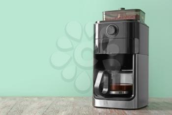 Modern coffee machine on table against color background�