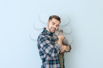 Young man with cute funny cat on light background�