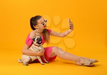 Teenage girl taking selfie with cute pug dog on color background�