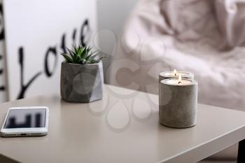 Beautiful burning candles, succulent and mobile phone on table in room�
