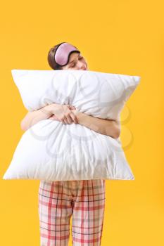 Young woman with pillow and sleep mask on color background�