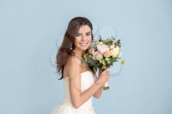 Beautiful young bride with bouquet of flowers on color background�