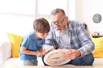 Grandfather teaching little boy to repair clock at home�