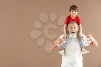 Funny little boy with grandfather on color background�
