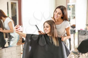 Young woman taking selfie with her hairdresser in salon�
