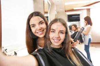 Young woman taking selfie with her hairdresser in salon�
