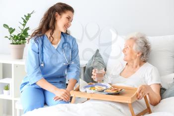 Young caregiver bringing senior woman breakfast in bed�