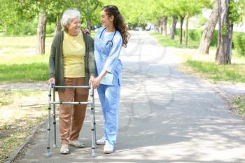 Caregiver walking with senior woman in park�