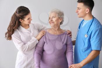 Young medical workers with senior woman on grey background�