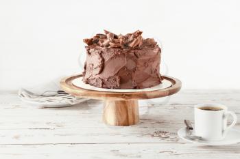 Stand with tasty chocolate cake and cup of coffee on table�