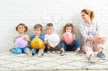 Cute little children with nursery teacher and air balloons sitting near white brick wall�