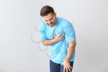 Young man suffering from heart attack on light background�