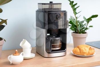 Modern coffee machine, cups and croissants on kitchen table�
