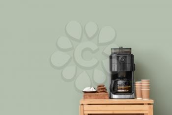 Modern coffee machine, cups, cookies and sugar on table against color background�
