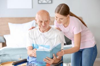 Young woman reading book with her father in nursing home�