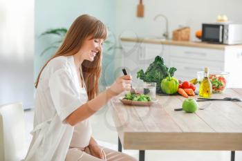 Beautiful pregnant woman eating healthy salad in kitchen�