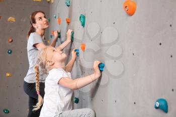 Young woman with her little daughter climbing wall in gym 