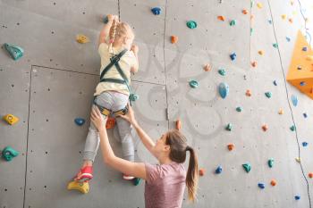 Instructor helping little girl to climb wall in gym�