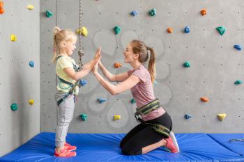 Little girl and instructor giving each other high-five in climbing gym�