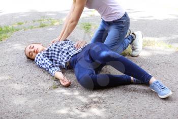Female passer-by doing CPR on unconscious woman outdoors�