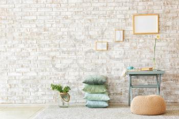 Table, pouf and soft pillows near brick wall�