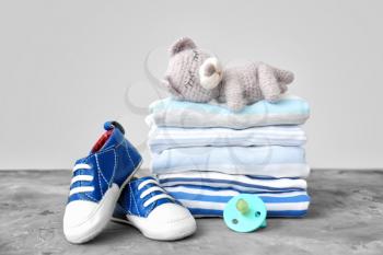 Stack of baby clothes, shoes, toy and pacifier on table�