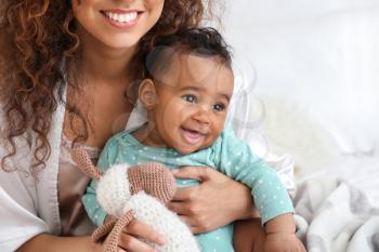 Happy African-American mother with cute little baby in bedroom�