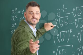 Handsome math teacher writing on blackboard in classroom�