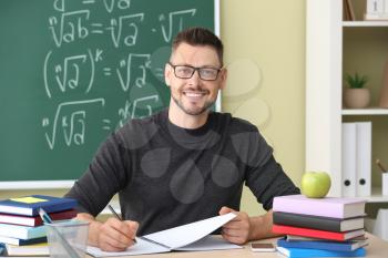 Handsome male teacher sitting at table in classroom�