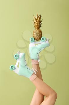 Legs of woman in roller skates and with golden pineapple on color background�