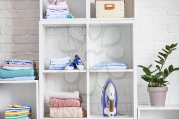 Rack with stacks of clean clothes and iron at home�