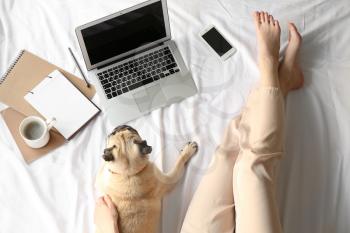 Young woman with laptop and cute pug dog resting on bed�