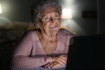Senior woman using laptop at night�