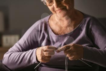 Senior woman knitting at home late in evening�