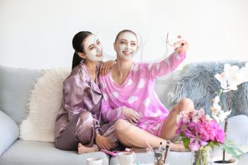 Beautiful young women with facial masks taking selfie at home�