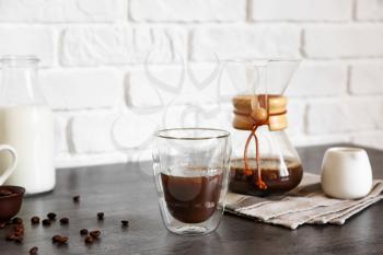 Glass of hot coffee on table near brick wall�