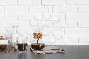 Glass and chemex of hot coffee on table near brick wall�